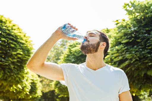 man drinks from a bottle of water in the hot sun