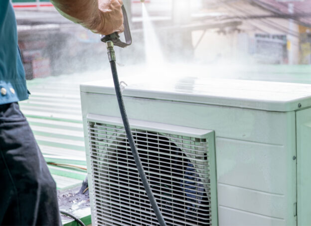 A person using a power washer to clean the inside of an AC unit