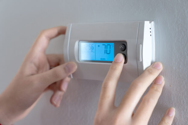 A person turning the thermostat to 70 degrees F