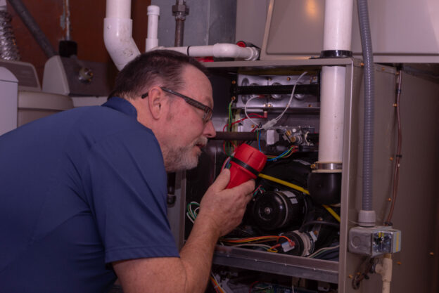 Man with flashlight examining the wiring and other components inside of a furnace